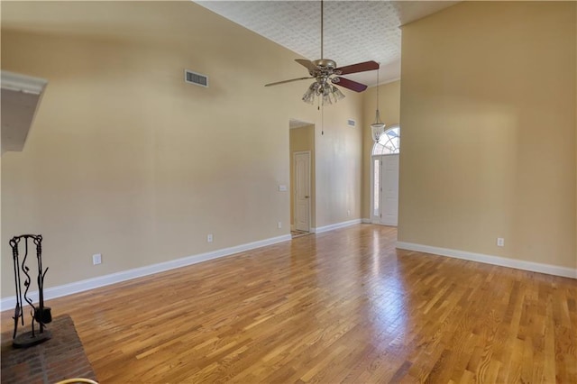 spare room featuring visible vents, baseboards, a ceiling fan, a towering ceiling, and light wood-style flooring