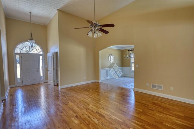 foyer featuring visible vents, arched walkways, wood finished floors, crown molding, and ceiling fan with notable chandelier