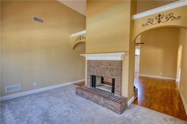 carpeted living area with a brick fireplace, visible vents, and a towering ceiling