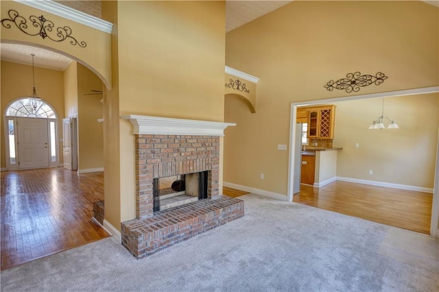 unfurnished living room featuring a towering ceiling, carpet, a fireplace, and wood finished floors