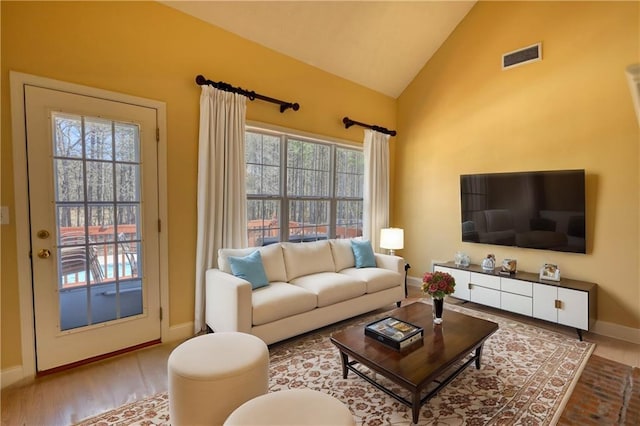 living area with lofted ceiling, visible vents, baseboards, and wood finished floors