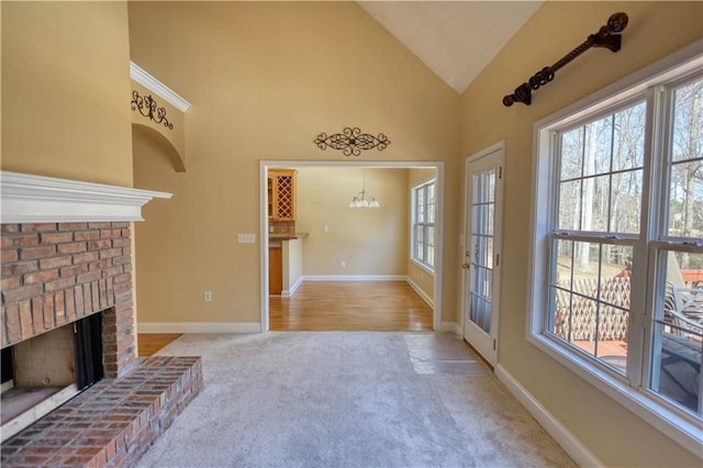 interior space featuring a chandelier, high vaulted ceiling, light carpet, a fireplace, and baseboards