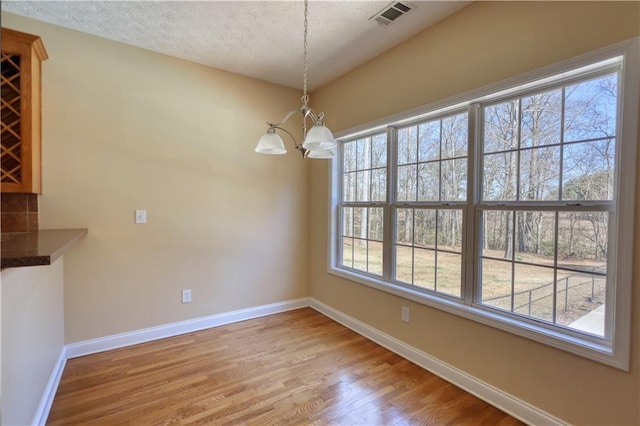 unfurnished dining area with baseboards, visible vents, light wood-style flooring, a textured ceiling, and a notable chandelier