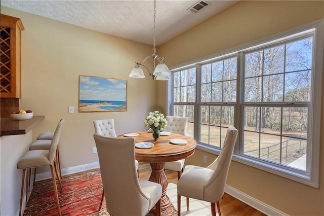 dining space featuring baseboards, visible vents, wood finished floors, a textured ceiling, and a notable chandelier