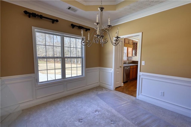 unfurnished dining area featuring a wainscoted wall, crown molding, visible vents, an inviting chandelier, and carpet flooring