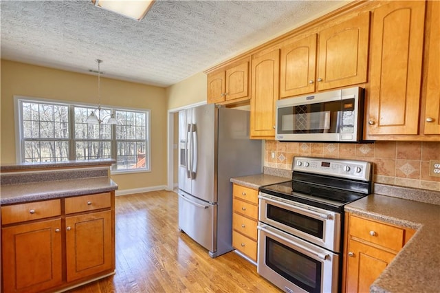 kitchen with pendant lighting, appliances with stainless steel finishes, light wood-style floors, and decorative backsplash