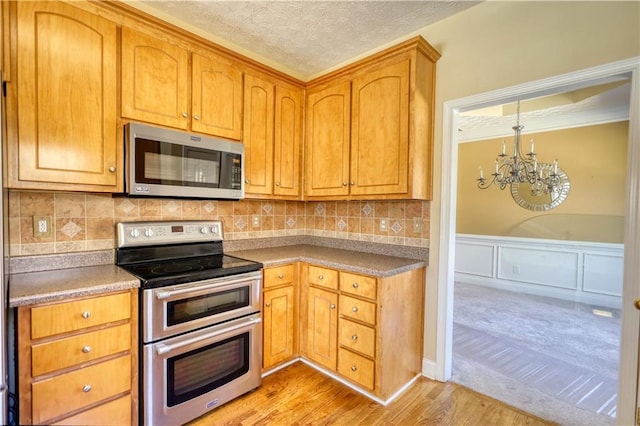 kitchen featuring wainscoting, appliances with stainless steel finishes, a textured ceiling, light wood-style floors, and a chandelier