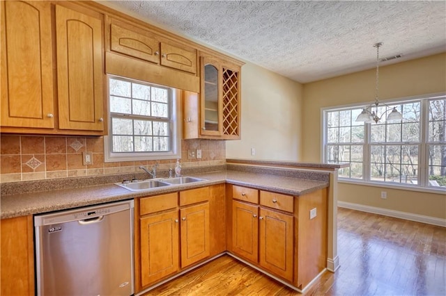 kitchen with visible vents, brown cabinetry, dishwasher, a peninsula, and a sink