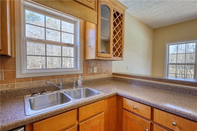 kitchen featuring glass insert cabinets, brown cabinetry, a sink, and a textured ceiling