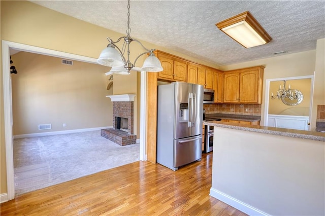 kitchen with a notable chandelier, visible vents, appliances with stainless steel finishes, a brick fireplace, and light wood-type flooring