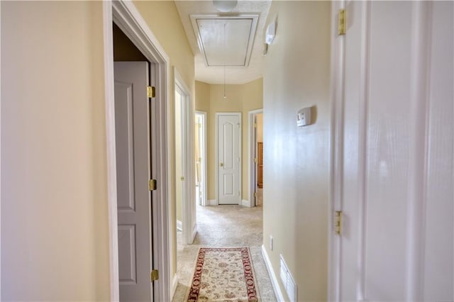 hall featuring visible vents, light colored carpet, attic access, and baseboards