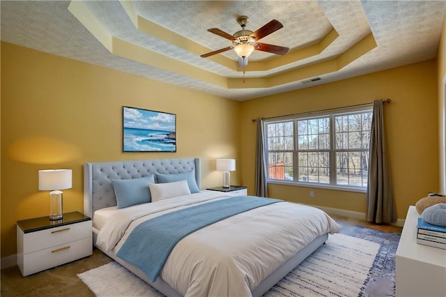 carpeted bedroom with a textured ceiling, ceiling fan, visible vents, baseboards, and a tray ceiling