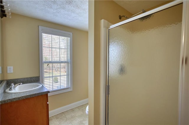 full bath with a stall shower, vanity, a textured ceiling, baseboards, and tile patterned floors