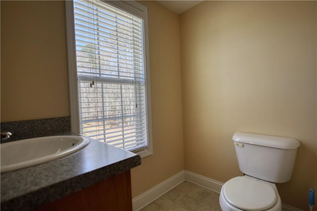 half bath featuring toilet, vanity, baseboards, and tile patterned floors