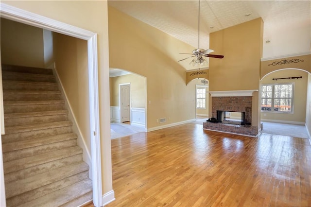 unfurnished living room featuring light wood-type flooring, a brick fireplace, stairs, and a towering ceiling