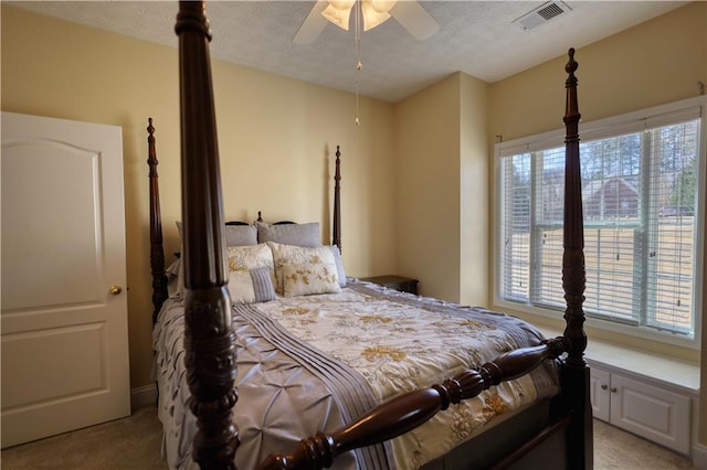 bedroom featuring a ceiling fan, visible vents, light carpet, and a textured ceiling