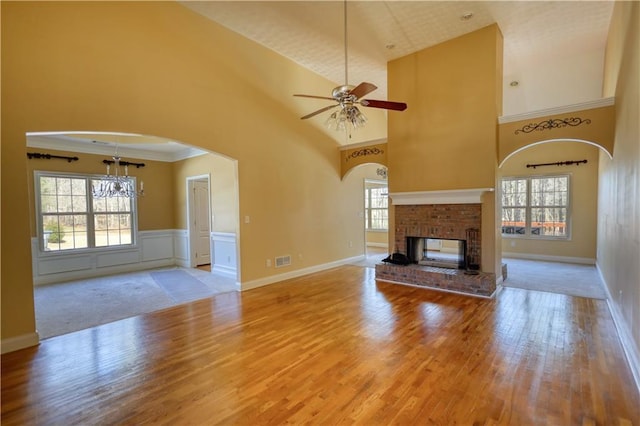 unfurnished living room featuring visible vents, a high ceiling, a ceiling fan, a brick fireplace, and wood finished floors