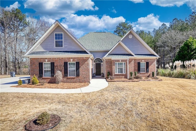 craftsman-style home featuring a front yard, brick siding, and roof with shingles