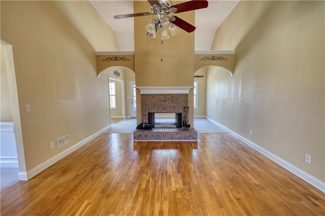 unfurnished living room with a fireplace, visible vents, arched walkways, and wood finished floors