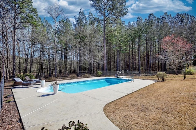 outdoor pool with a patio, fence, and a view of trees