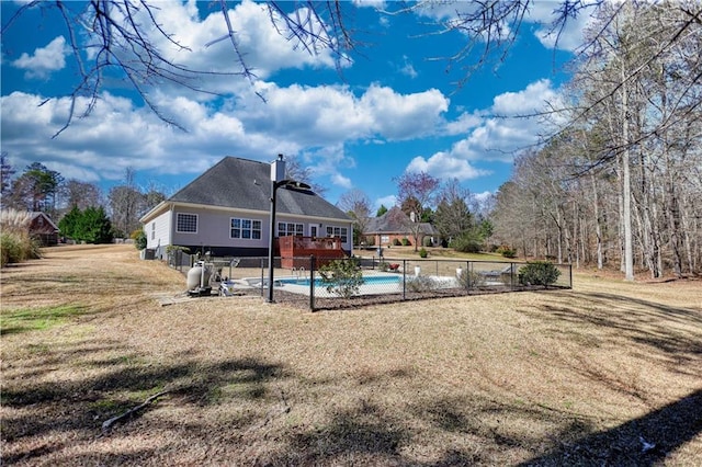 back of house featuring an outdoor pool, a lawn, a chimney, and fence