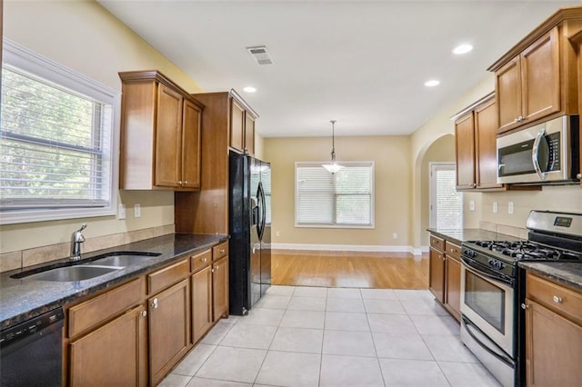 kitchen featuring brown cabinetry, arched walkways, black appliances, light tile patterned flooring, and a sink