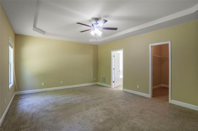 carpeted empty room featuring a raised ceiling, visible vents, baseboards, and ceiling fan