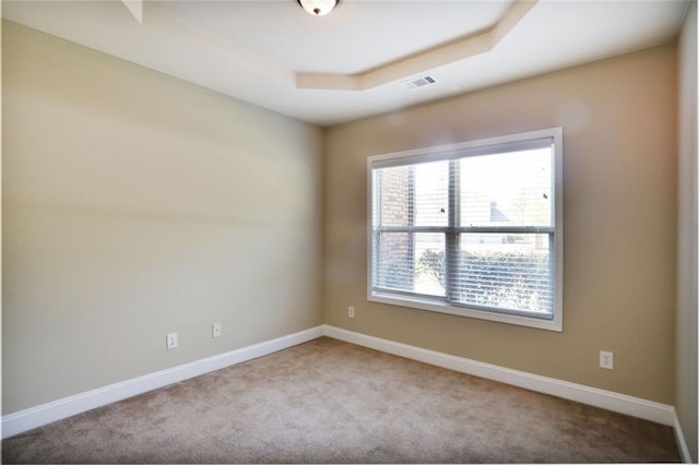 carpeted empty room with a tray ceiling, visible vents, and baseboards