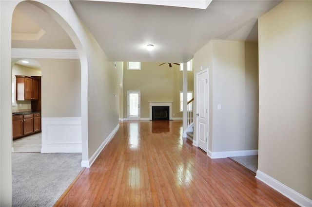 hall featuring light wood-style floors, baseboards, and arched walkways