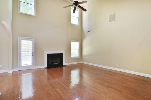 unfurnished living room featuring wood finished floors, a towering ceiling, a ceiling fan, and visible vents