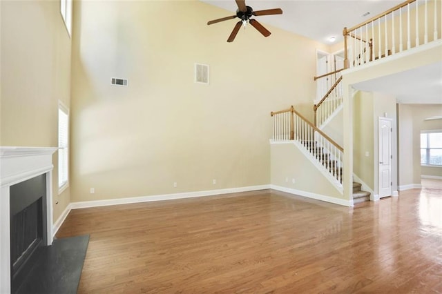 unfurnished living room with visible vents, a ceiling fan, a high ceiling, and a glass covered fireplace