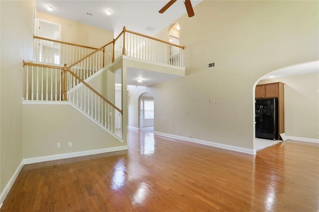 unfurnished living room featuring a ceiling fan, stairs, visible vents, arched walkways, and wood finished floors
