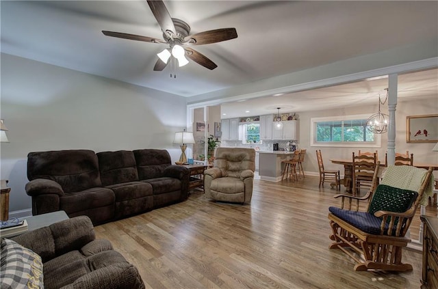 living room with ceiling fan with notable chandelier and light hardwood / wood-style floors