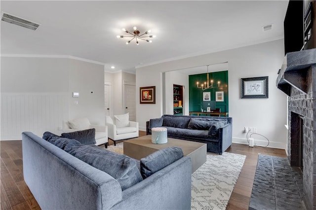 living room featuring visible vents, a brick fireplace, dark wood-style floors, an inviting chandelier, and crown molding