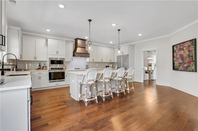 kitchen featuring a kitchen breakfast bar, custom exhaust hood, light countertops, stainless steel appliances, and a sink