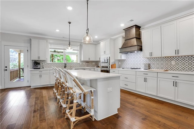 kitchen featuring stainless steel appliances, dark wood-style flooring, a kitchen island, light countertops, and custom exhaust hood