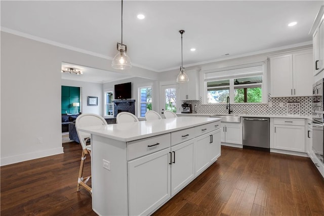 kitchen featuring stainless steel appliances, a sink, ornamental molding, decorative backsplash, and a kitchen bar