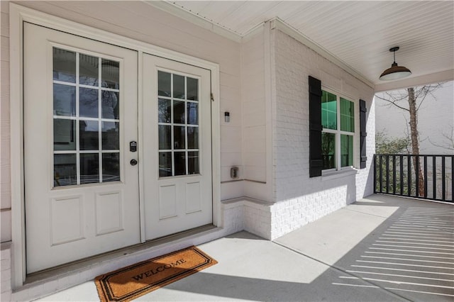 view of exterior entry with brick siding, a porch, and french doors