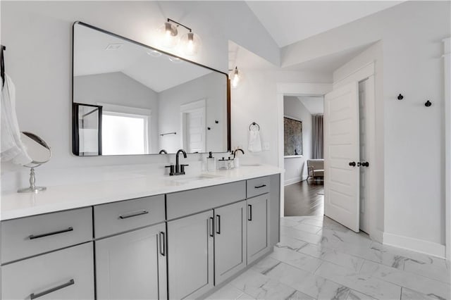 bathroom featuring double vanity, baseboards, lofted ceiling, marble finish floor, and a sink