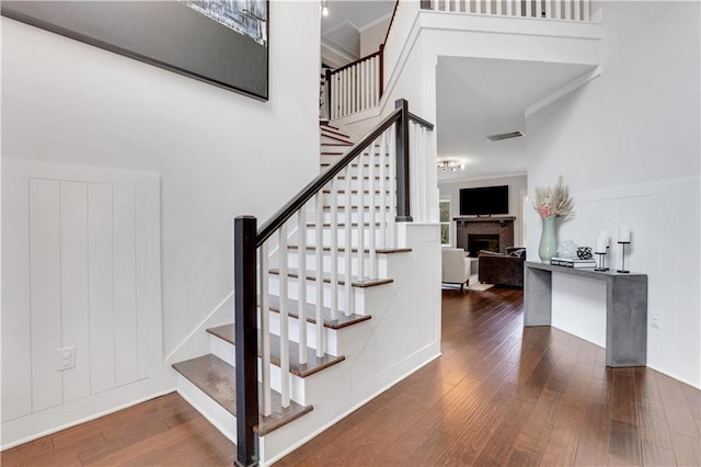 staircase featuring a fireplace, ornamental molding, and hardwood / wood-style floors