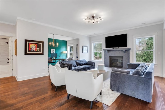 living area featuring dark wood-style floors, ornamental molding, a notable chandelier, and a glass covered fireplace