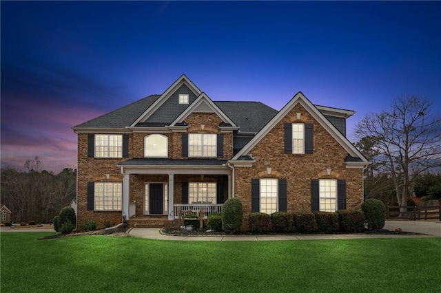 view of front of property featuring covered porch, brick siding, and a yard