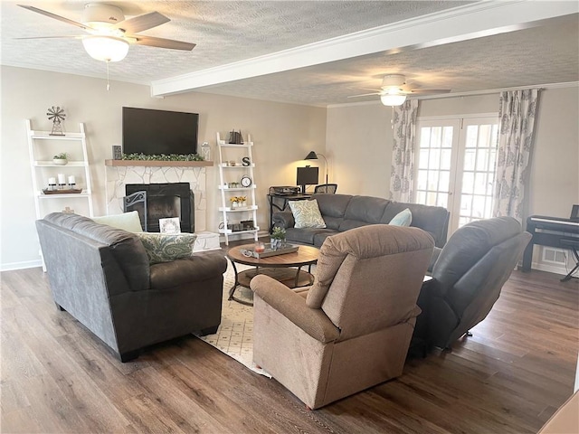 living room with a stone fireplace, a textured ceiling, ceiling fan, beam ceiling, and hardwood / wood-style floors