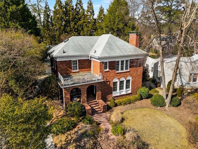 view of front of property featuring a porch, a chimney, brick siding, and a balcony