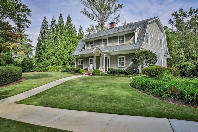 colonial inspired home featuring a front lawn, roof with shingles, and a gambrel roof