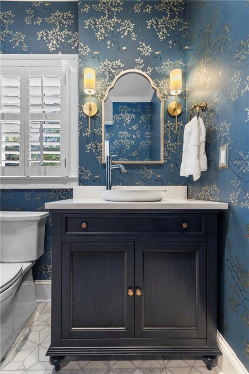 bathroom featuring toilet, wallpapered walls, baseboards, and vanity