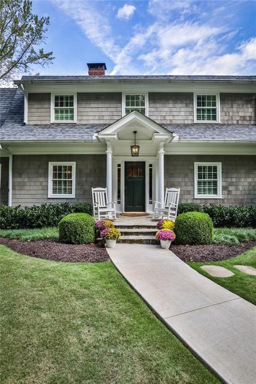 view of front facade with a front yard, roof with shingles, and a chimney