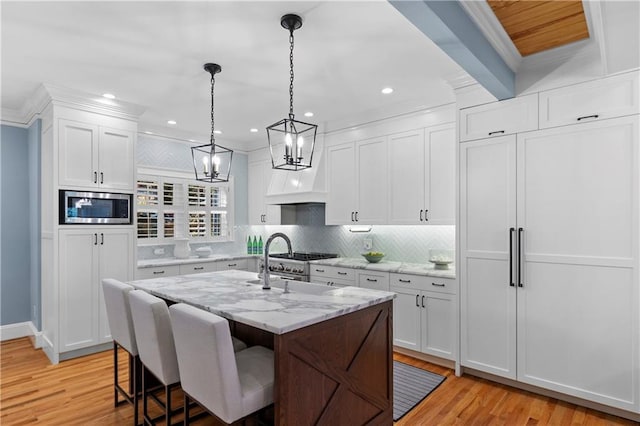 kitchen with light stone counters, a kitchen island with sink, white cabinetry, stainless steel microwave, and pendant lighting