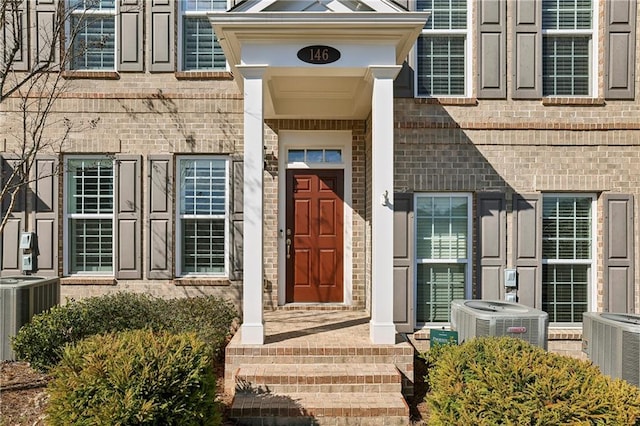 view of exterior entry featuring central AC unit and brick siding