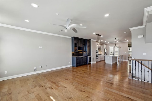 unfurnished living room with light wood-style floors, recessed lighting, ornamental molding, and ceiling fan with notable chandelier